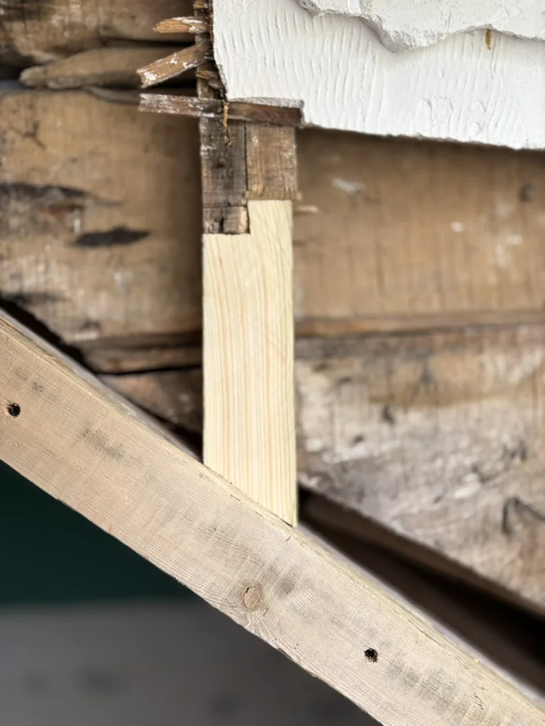 Gros plan d'une greffe de charpente : une pièce de bois saine aboutée à l'ancienne poutre pour reprendre la charge à l'about.