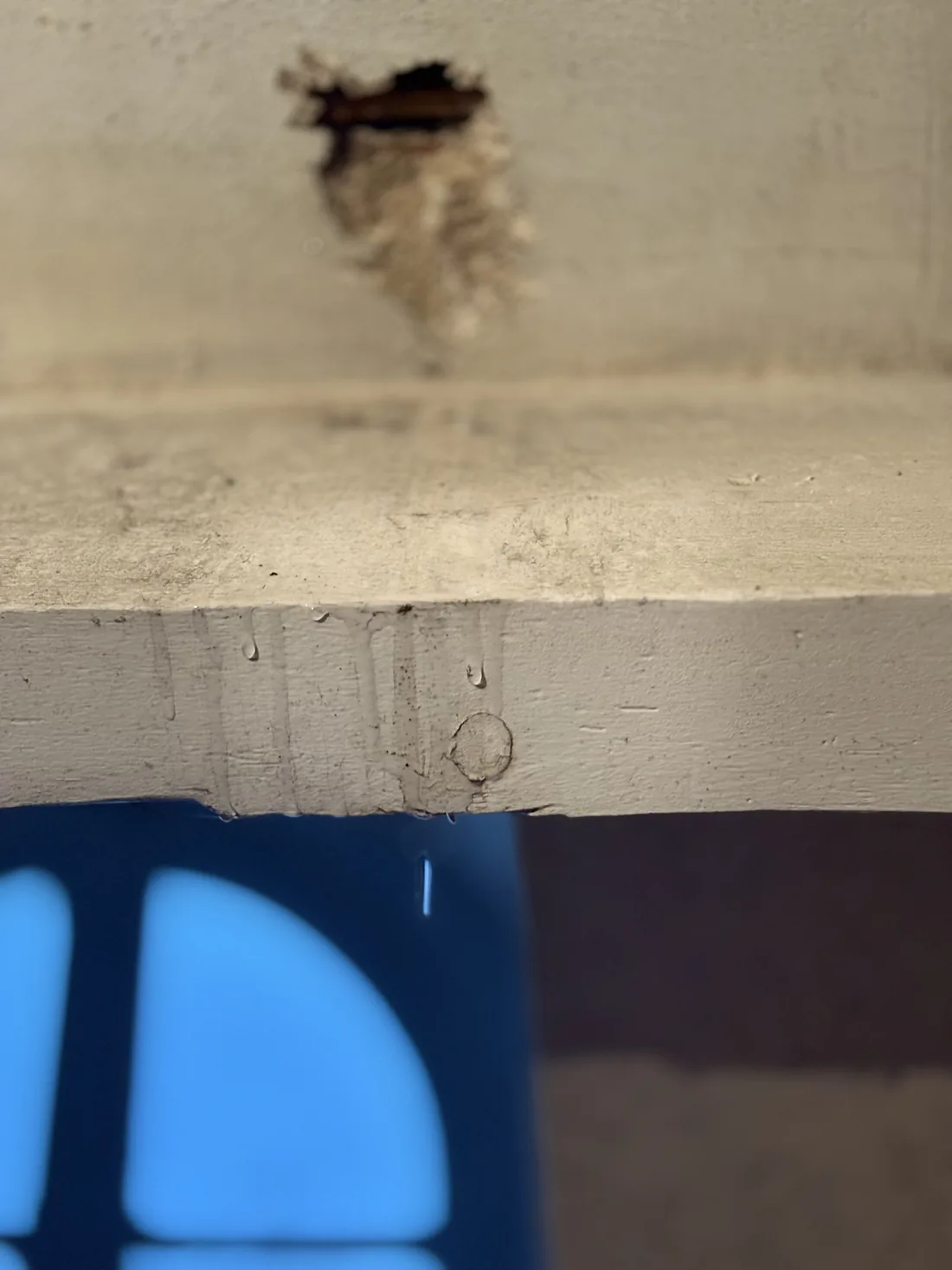 Eau d'infiltration s'écoulant le long d'une poutre de plafond et tombant goutte à goutte dans un seau, dans un manoir ancien.