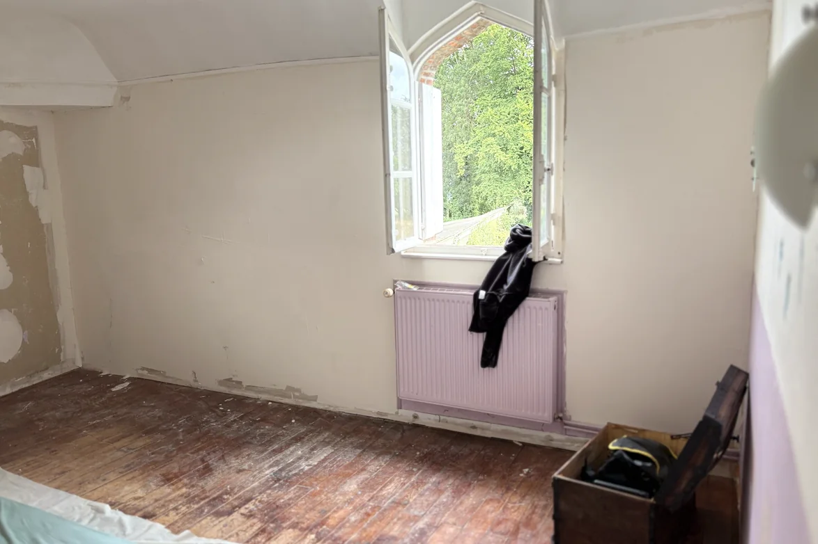Chambre d'un manoir ancien avant rénovation : fenêtre cintrée d'origine, radiateur, parquet terni et murs fatigués, future suite parentale.